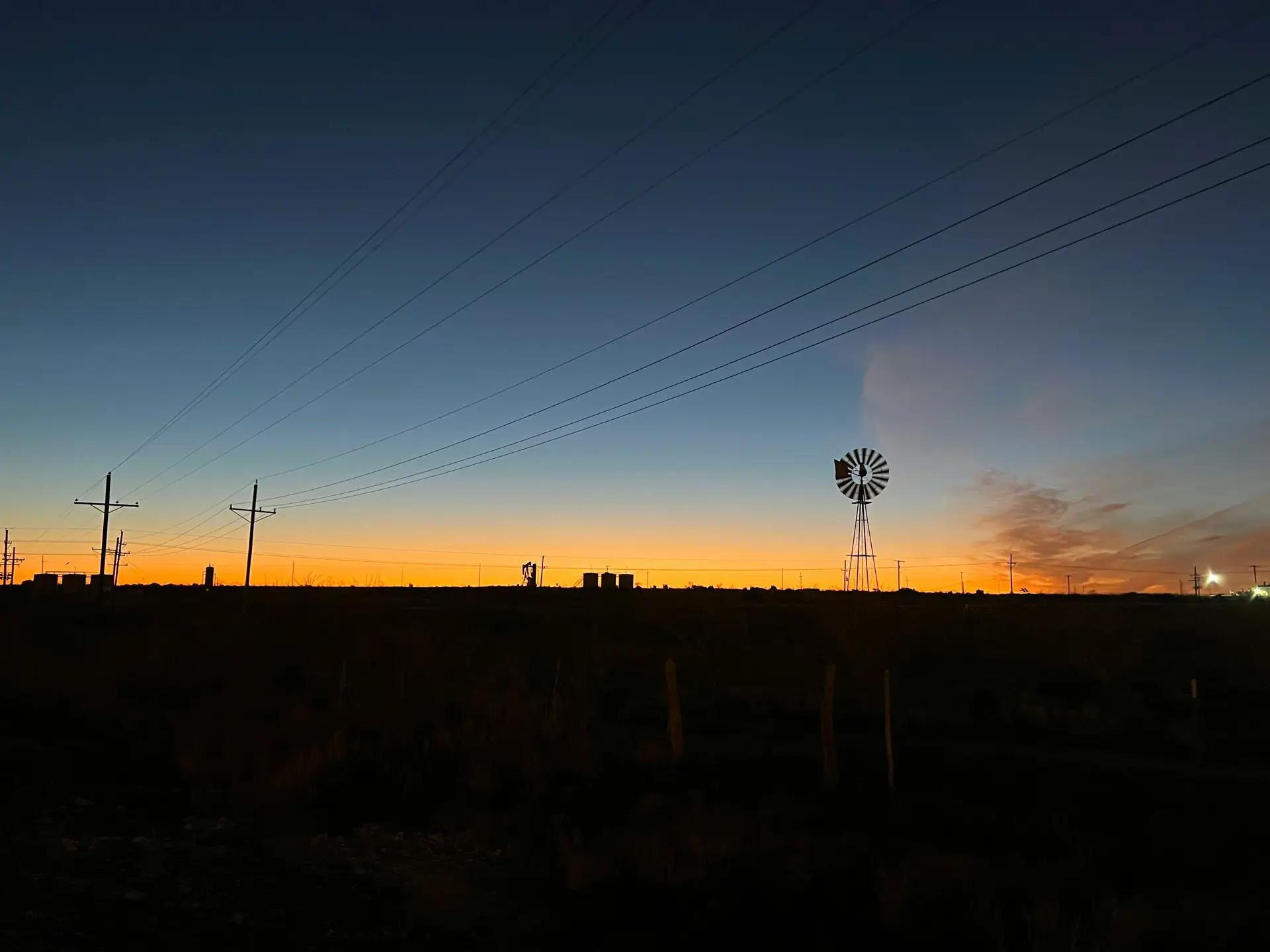 Pumpjack and windmill silhouetted against a dusk sky in the field