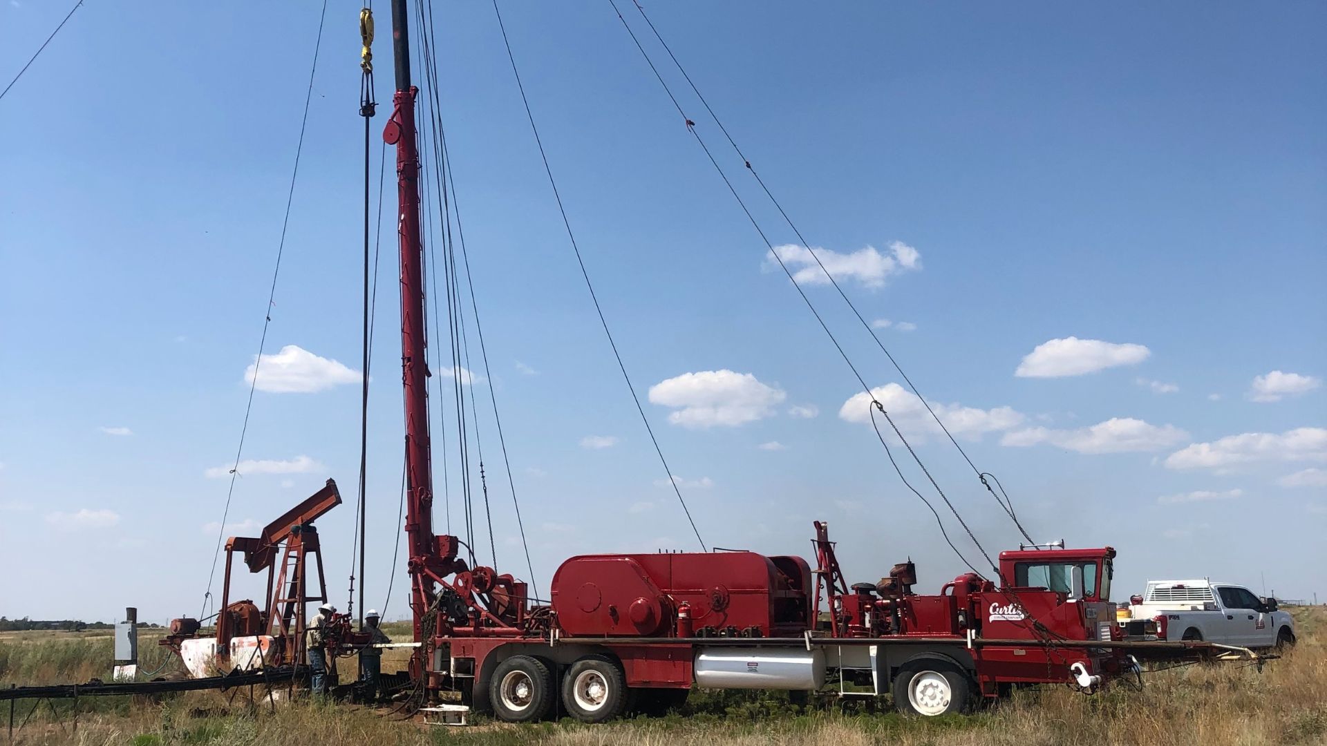 Workover rig servicing a well with pumpjack in the background