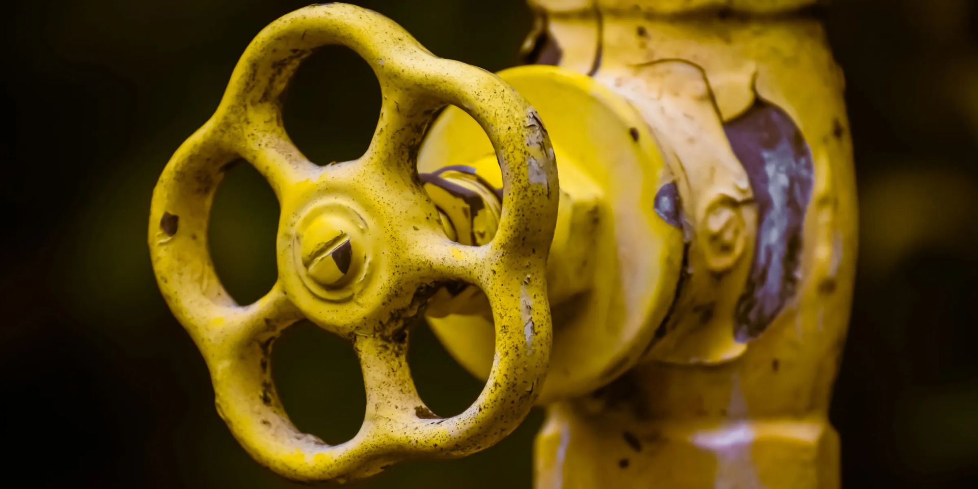 Close-up of a chipped yellow handwheel on a shut-off valve, the valve body painted the same yellow, against a dark background